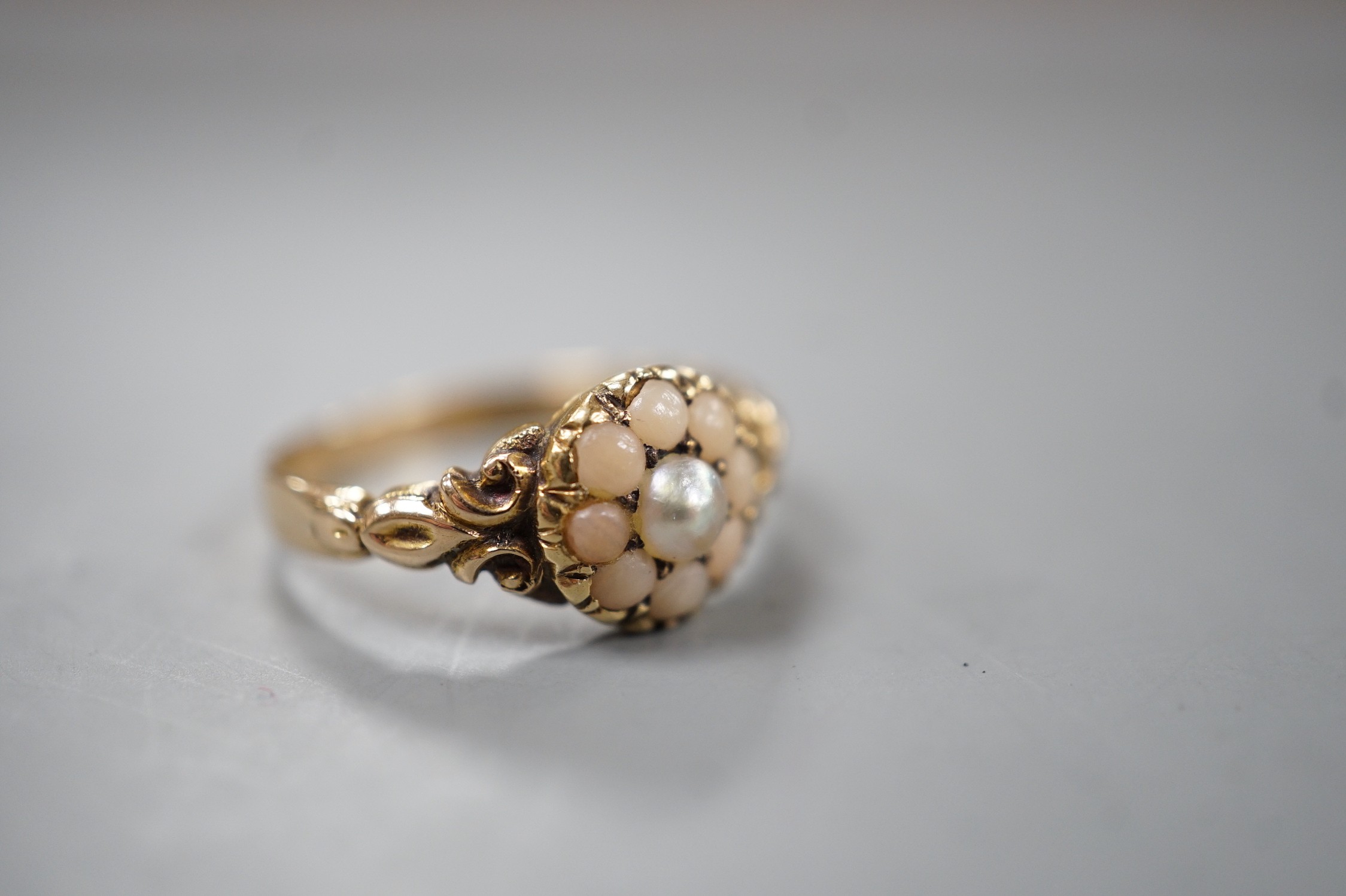 An early 20th century yellow metal, split coral and split pearl cluster set ring, size P, gross weight 2.5 grams.